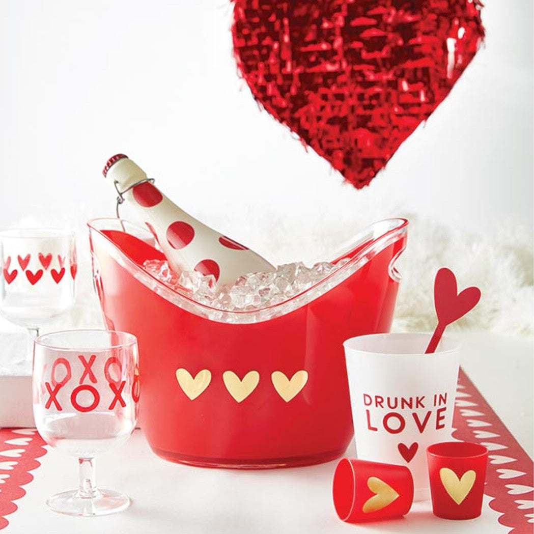 Valentine's Day-themed party setup with red bucket, glasses, and heart drink stirrers.