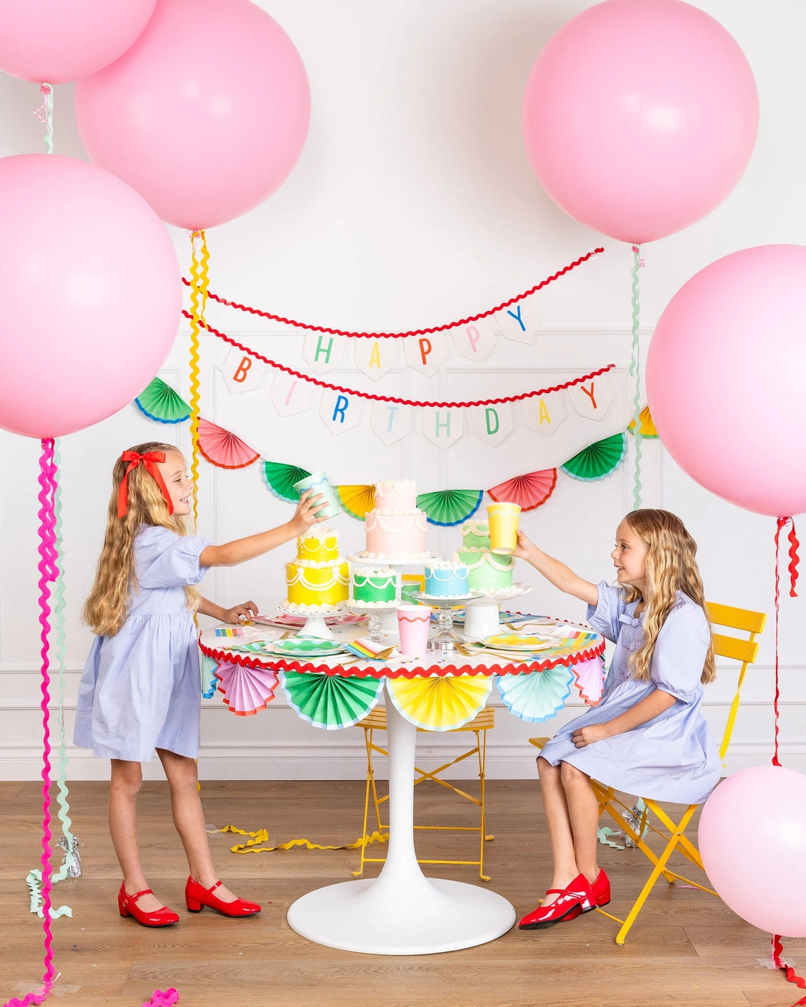 Two children at a birthday party with balloons and a cake.
