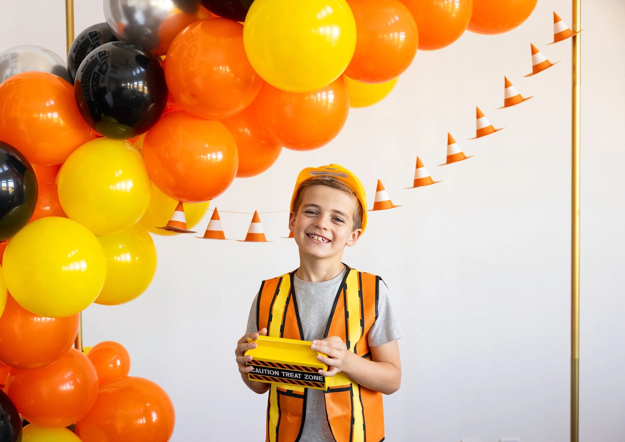 Child in a construction-themed outfit with balloons and a traffic cones banner in the background