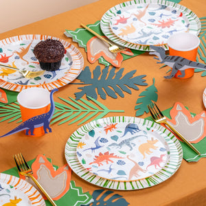Dinosaur-themed party table setting with plates, napkins, and cup stickers.