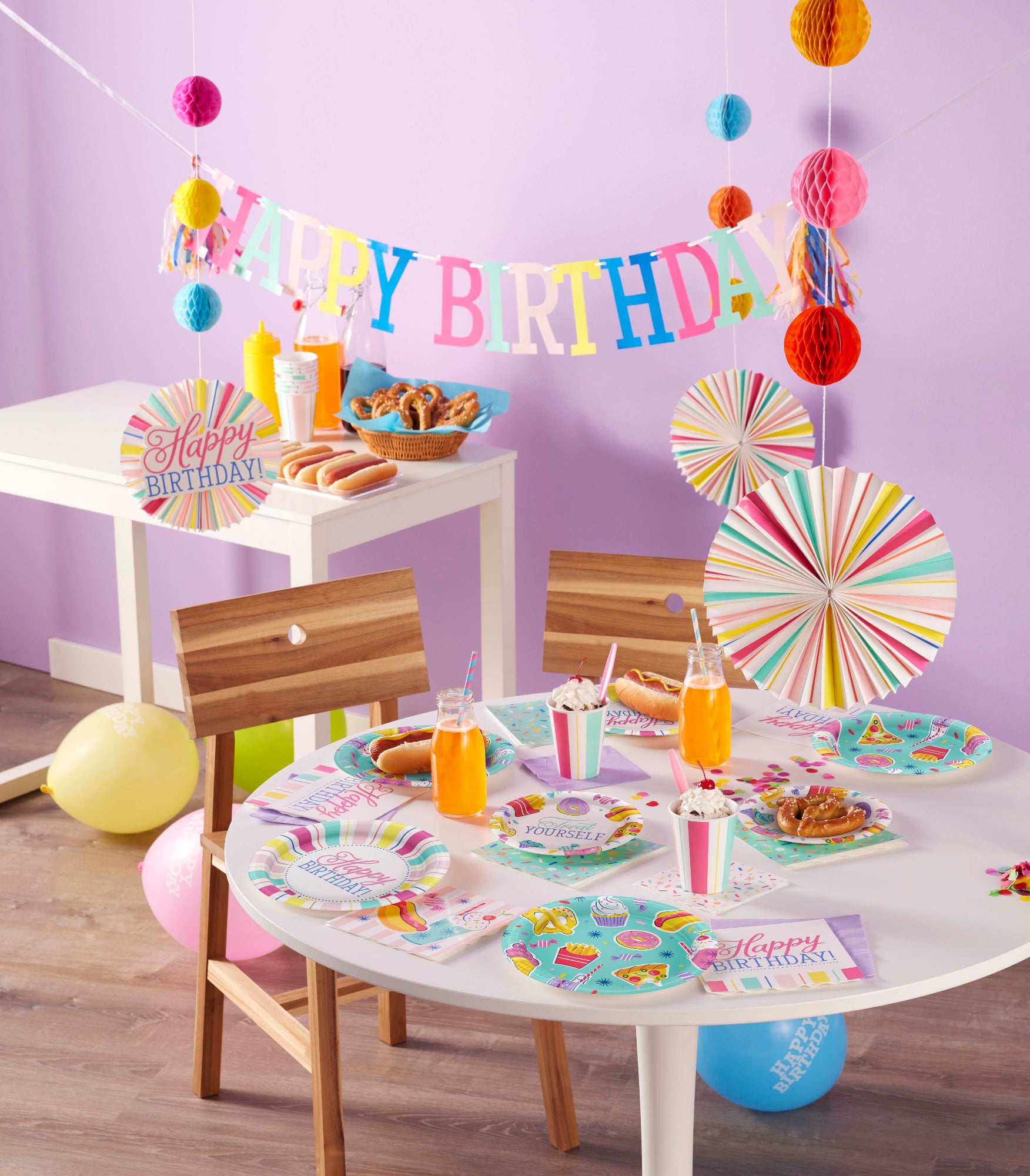 Children's birthday party setup with table, chairs, and decorations against a purple wall.
