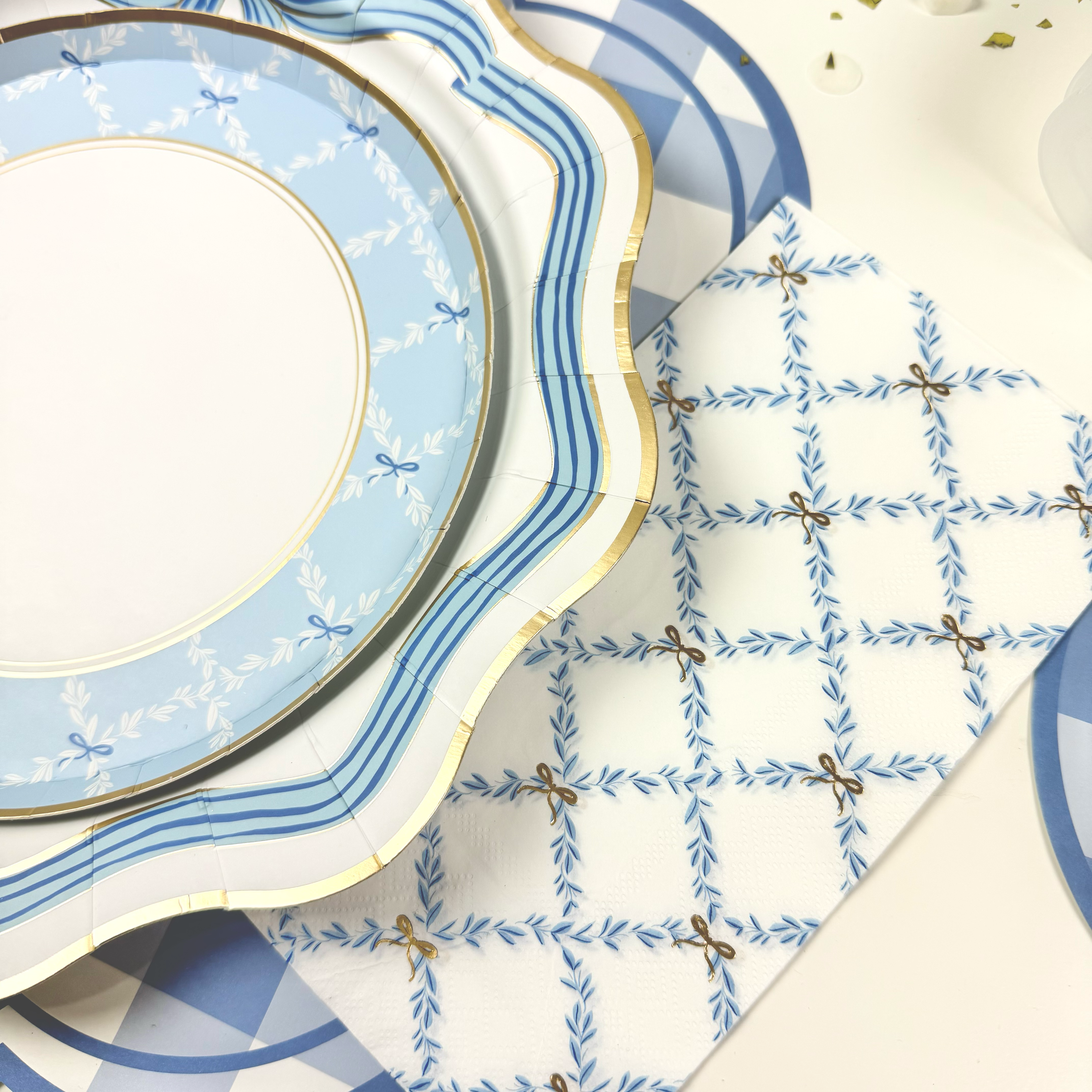 White guest towels with a blue trellis and gold bow pattern beside layered blue and gold plates.
