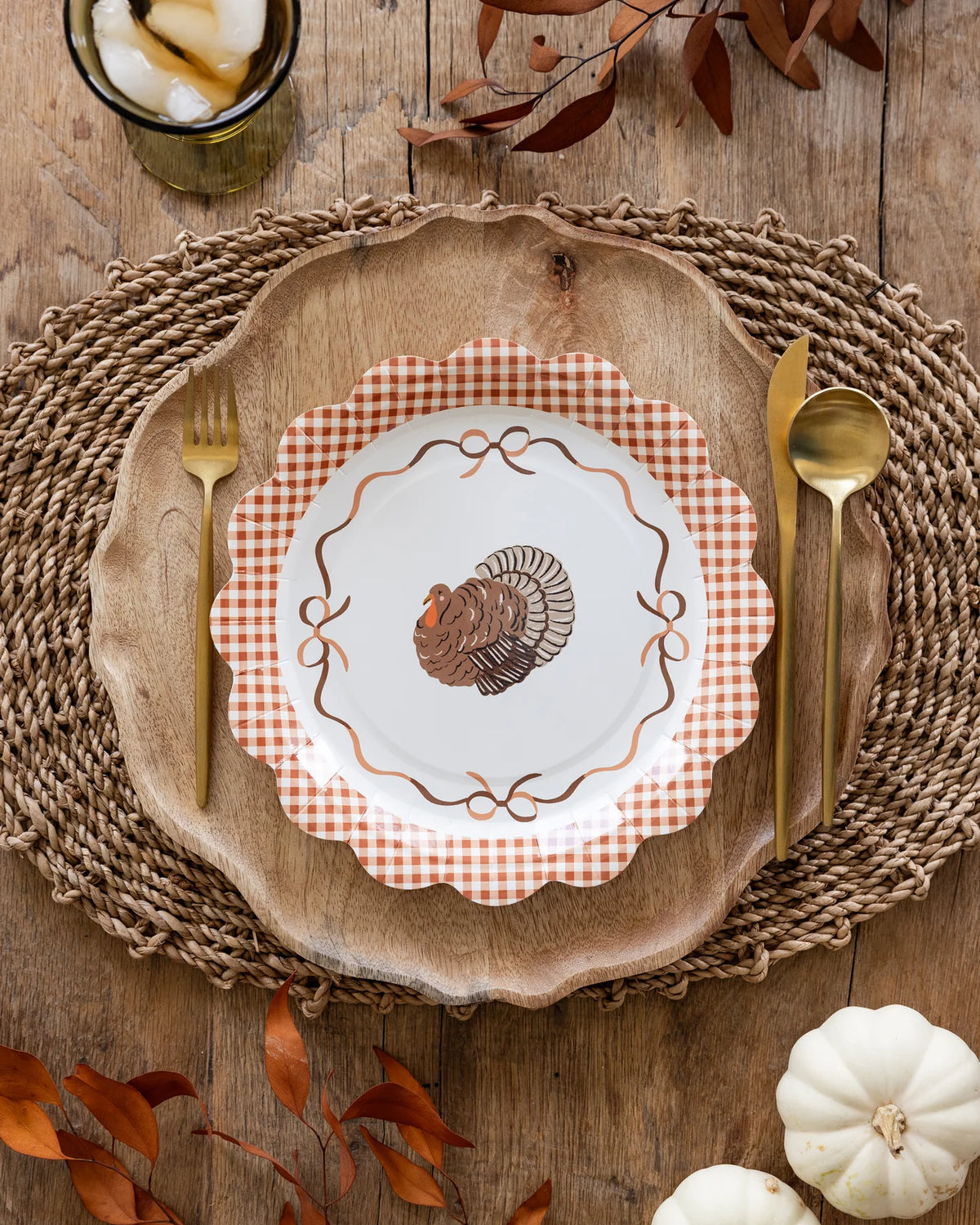 A paper plates with Brown and white gingham scalloped edged and a turkey in the center surrounded by four bows.