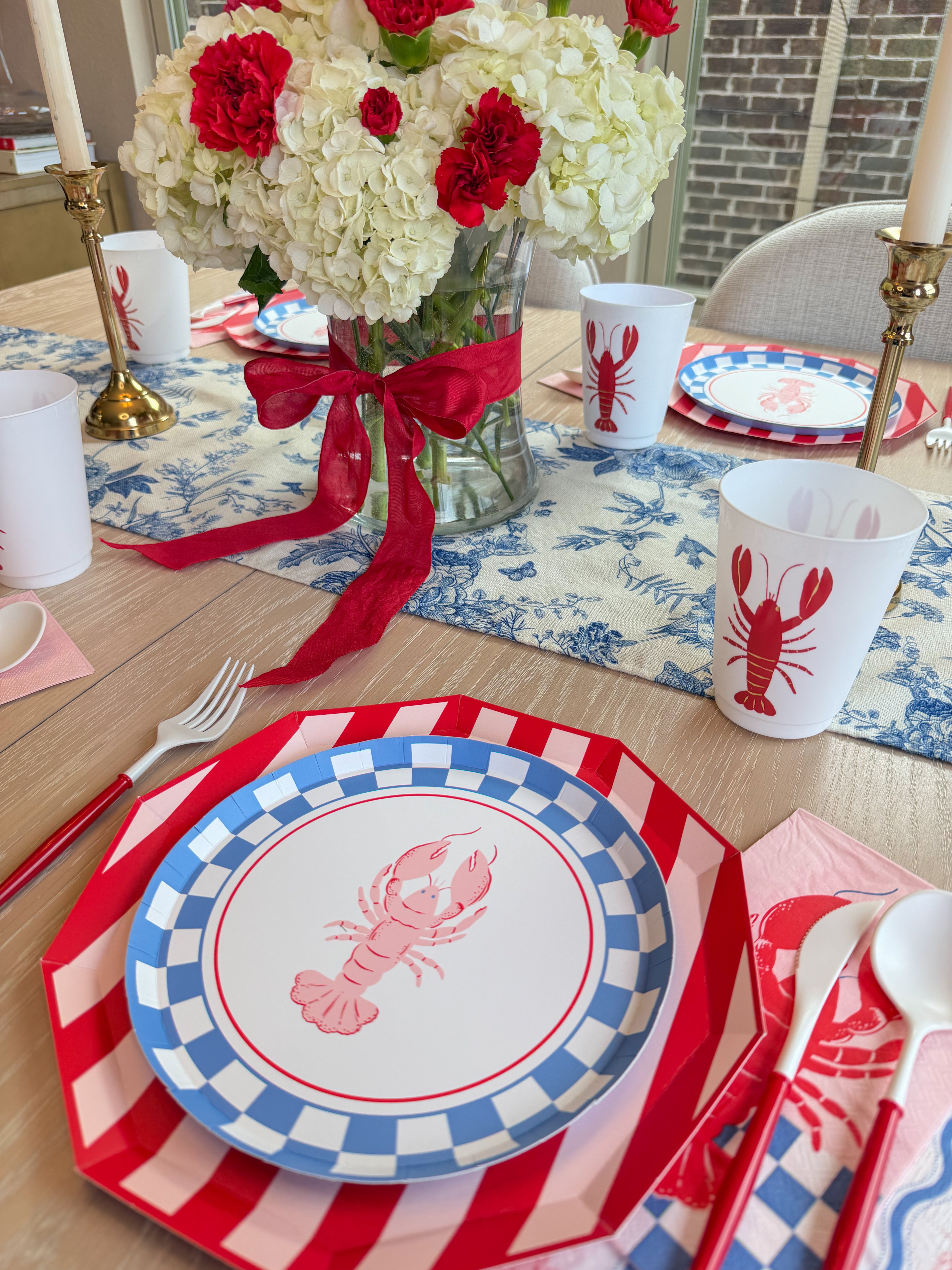 Red, white, and blue lobster-themed place setting with striped charger, checkered plate, lobster napkin, and matching cup.