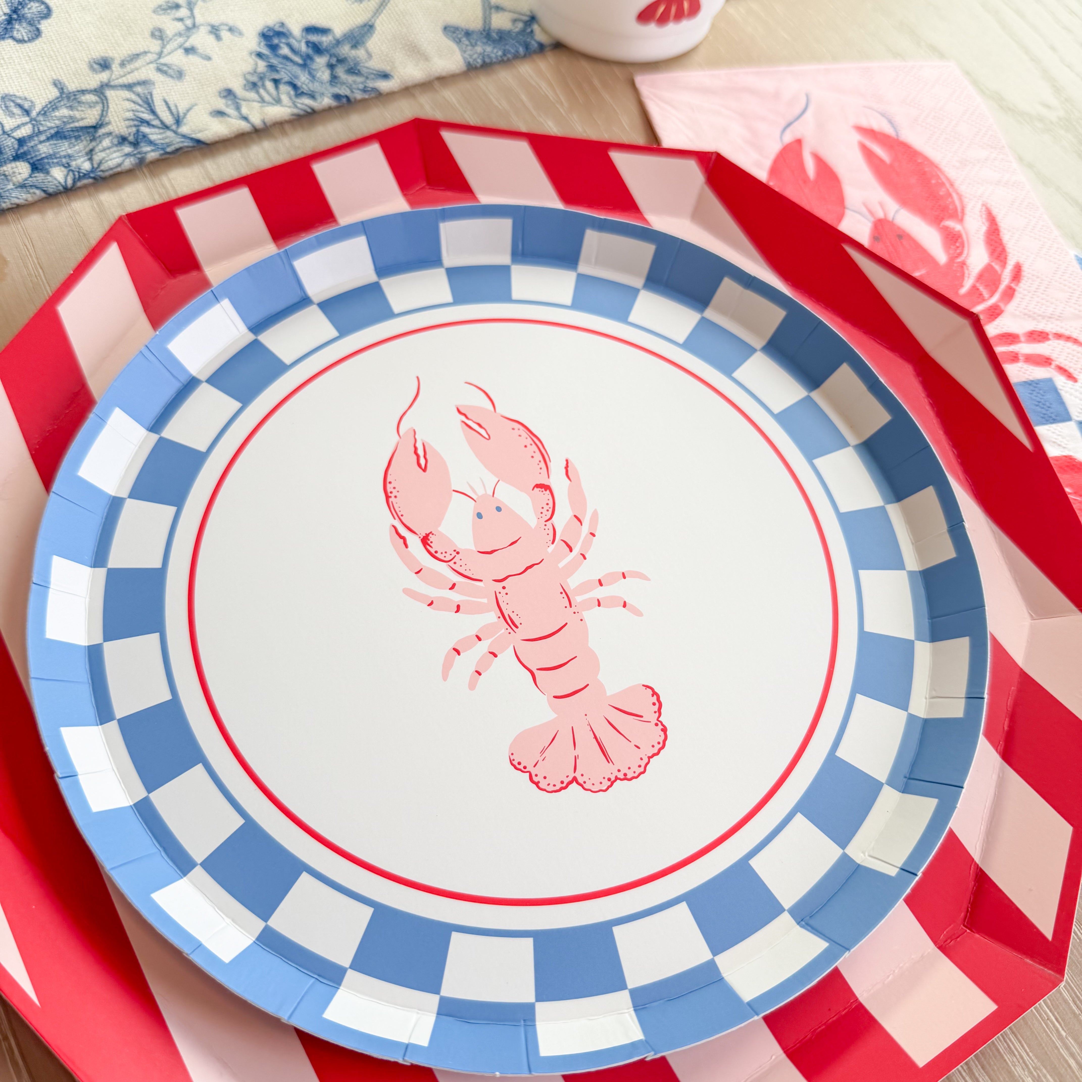 Close-up of lobster party plates layered on a red striped charger with coordinating lobster napkin and cup.