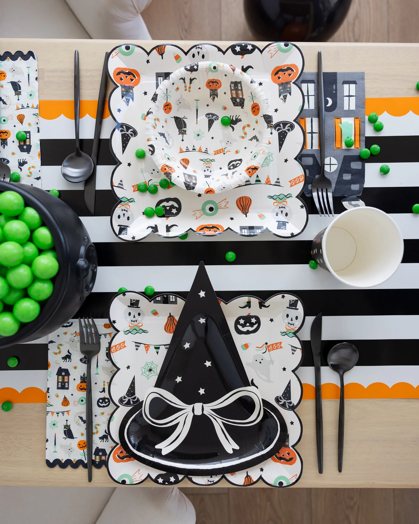 Halloween party table setting with decorative Halloween plates and utensils on a striped orange and black paper tablecloth.