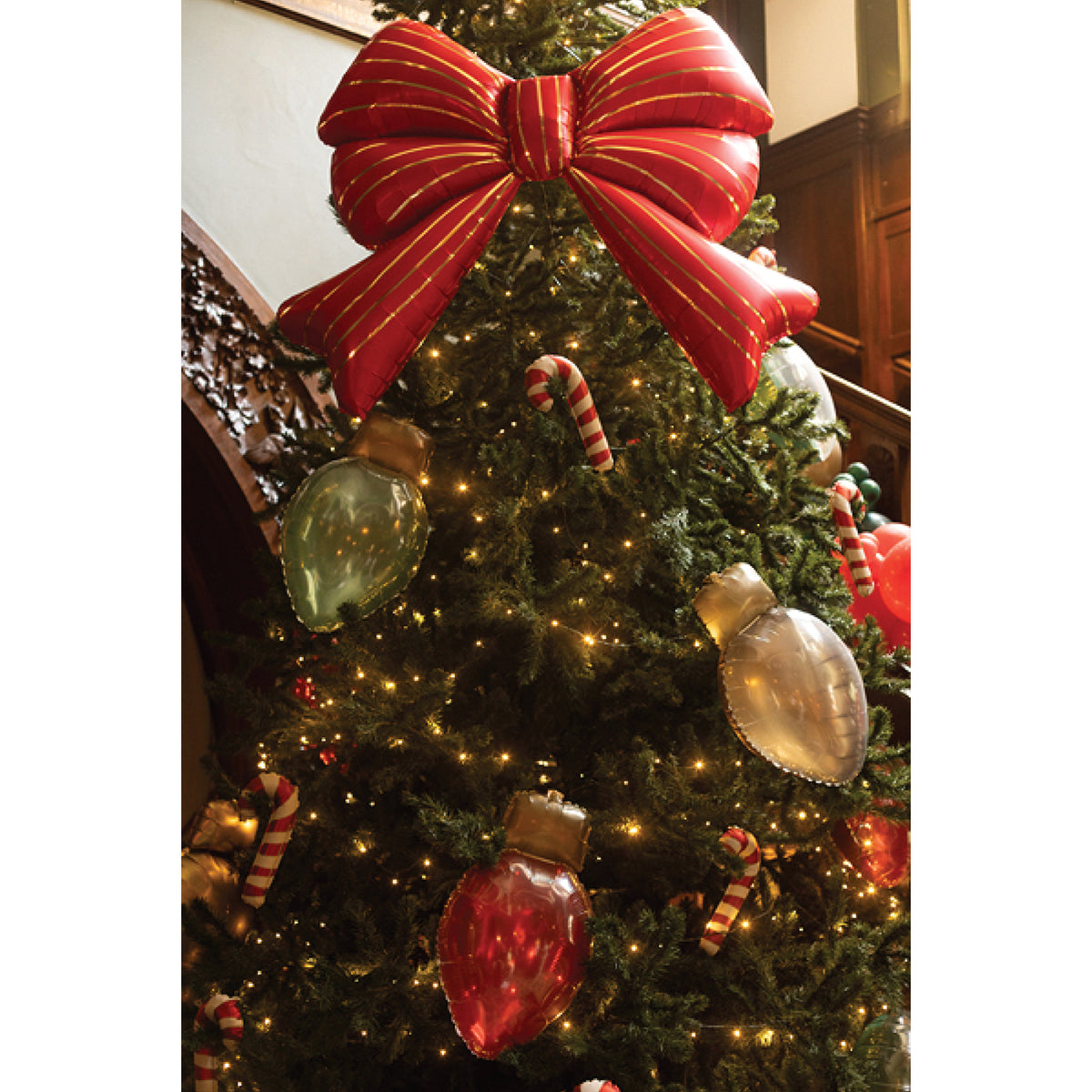 Red Christmas bow foil balloon with oversized ribbon loops, a gathered center, and flowing ribbon tails.