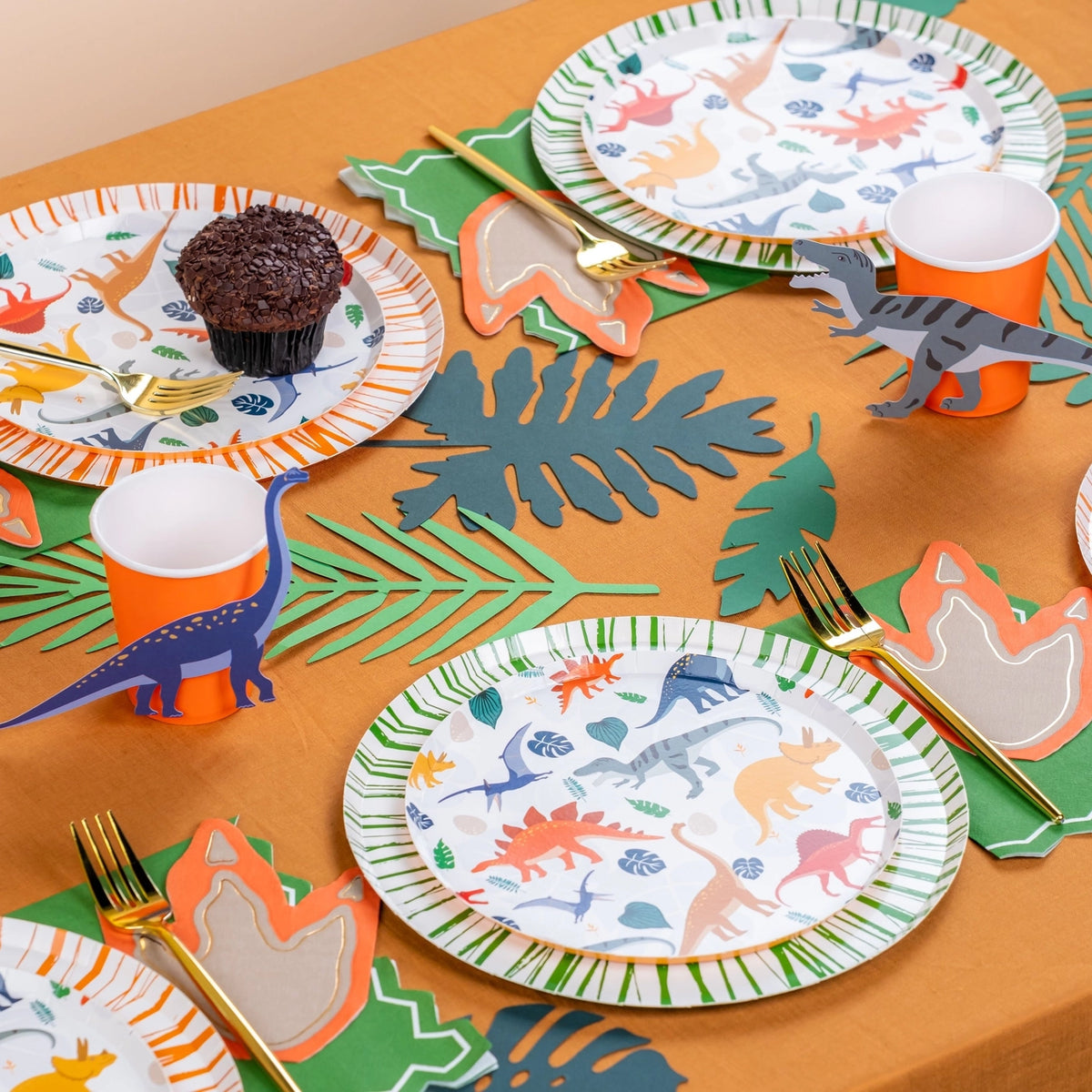 Dinosaur-themed party table setting with plates, napkins, and cup stickers.