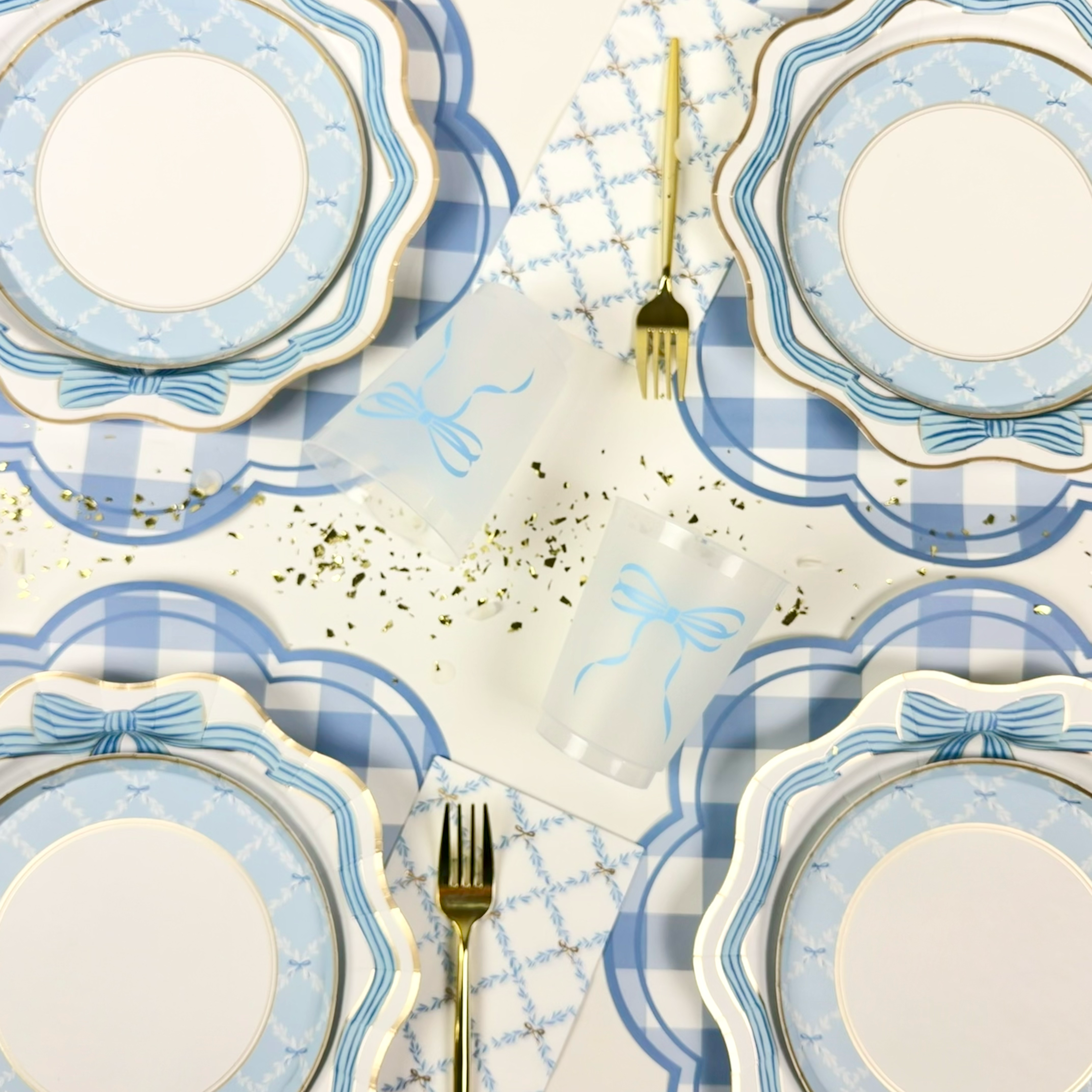 Blue bow paper plates with gold trim styled with a frosted bow cup and scattered gold confetti.