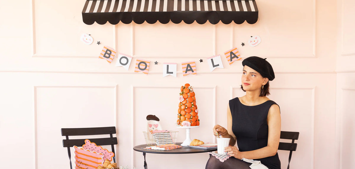 Woman sitting at a table with Halloween party decorations, including 'BOO LA LA' banner.