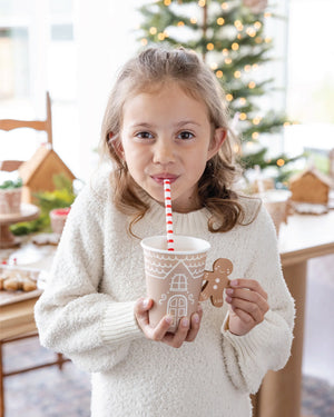 A child drinking out of a Gingerbread house paper cup with a gingerbread man handle