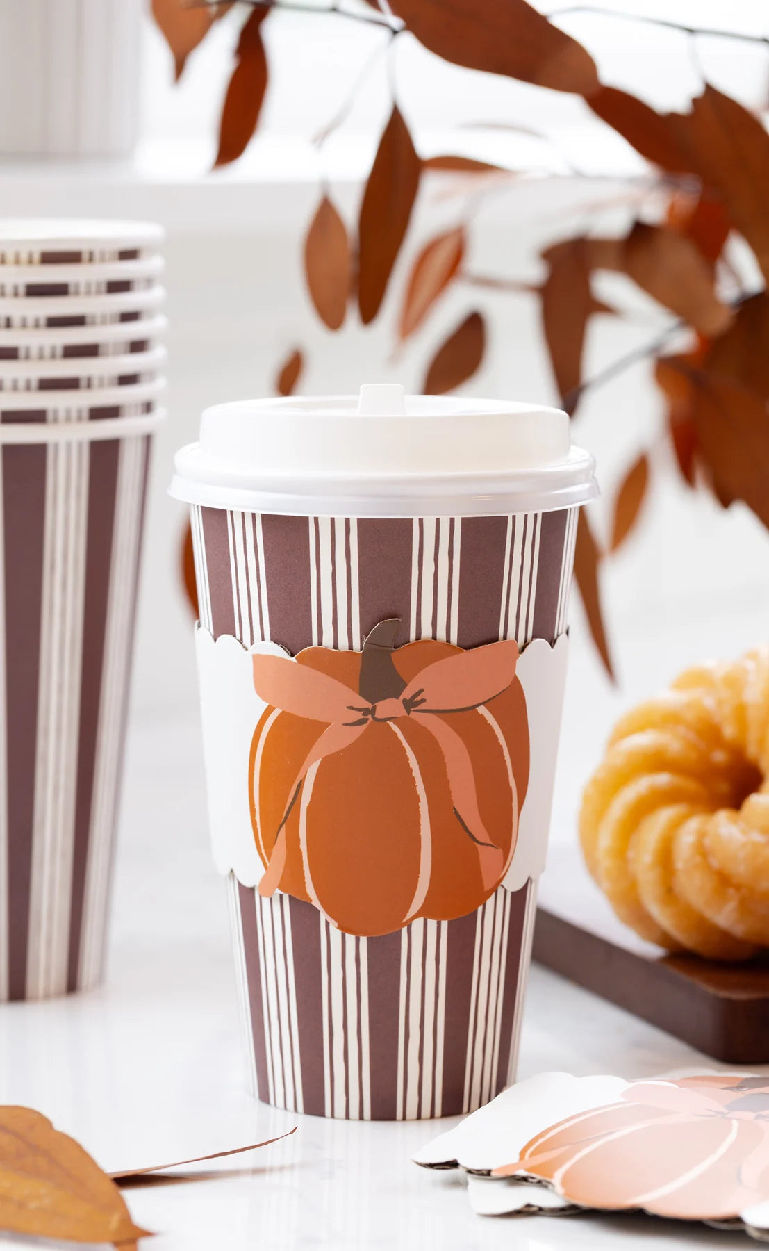 Brown striped paper coffee cups with a cardboard sleeve with a fall pumpkin with a bow