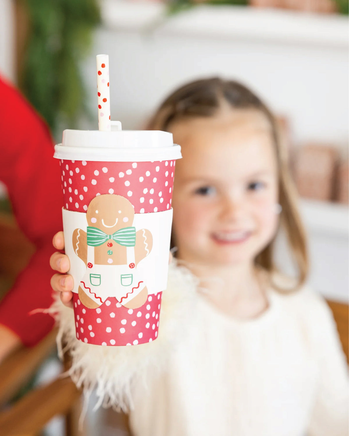 Child holding a festive red cup with a gingerbread man design