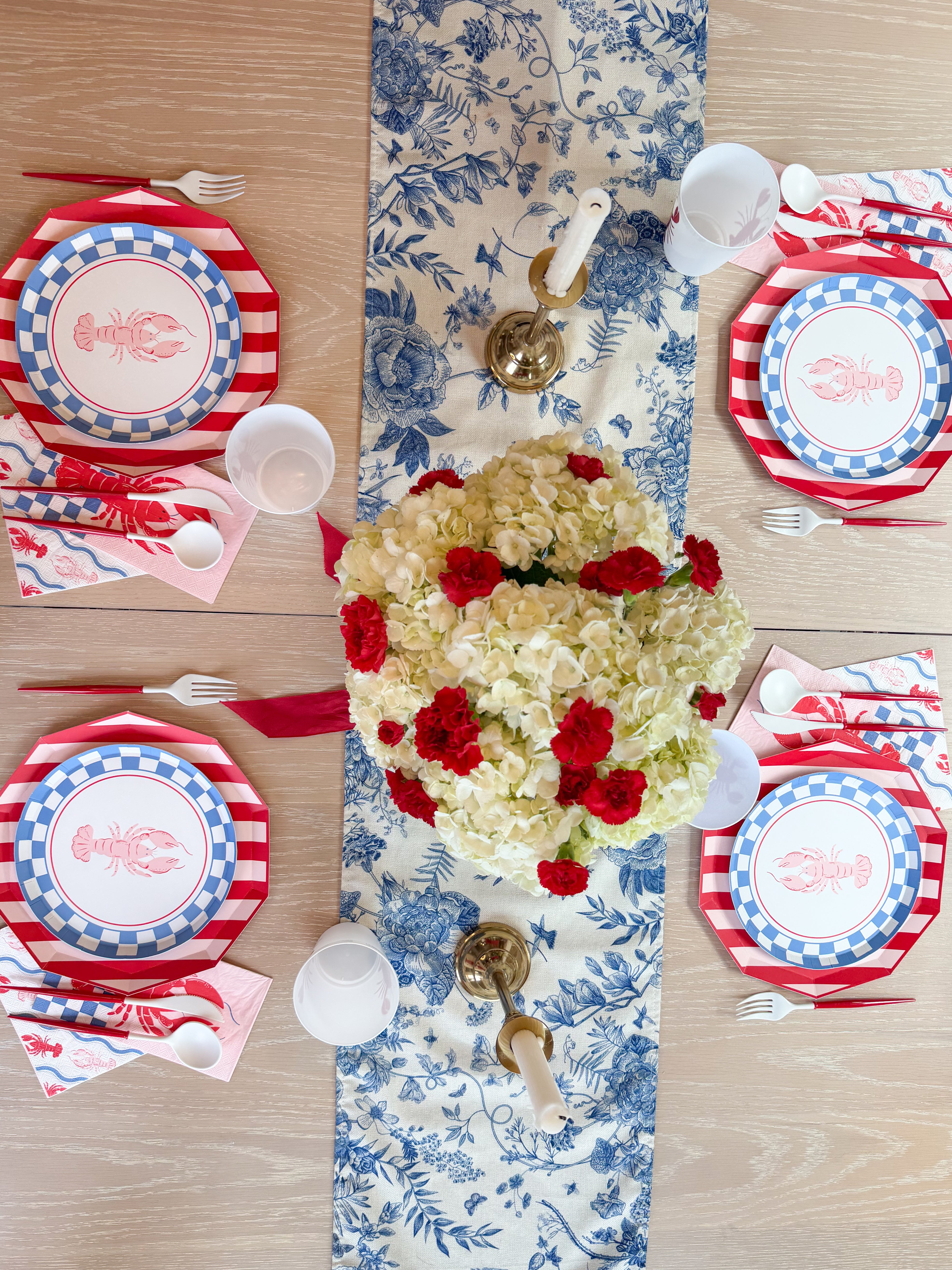 Lobster-themed table with hydrangea and red carnation centerpiece, striped plates, and nautical accents.