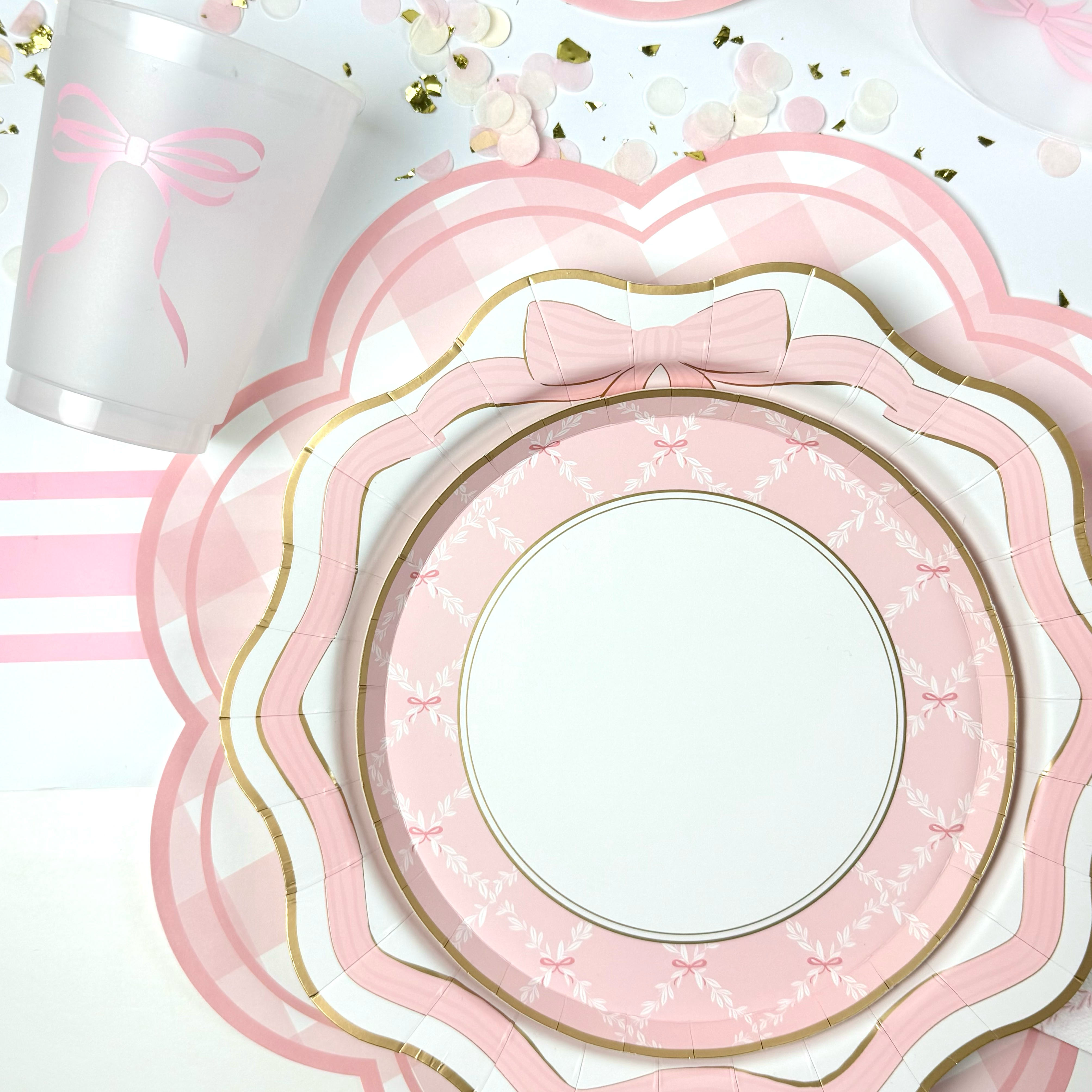 Close-up of pink scalloped plates with gold trim layered on a gingham placemat with a pink bow cup.