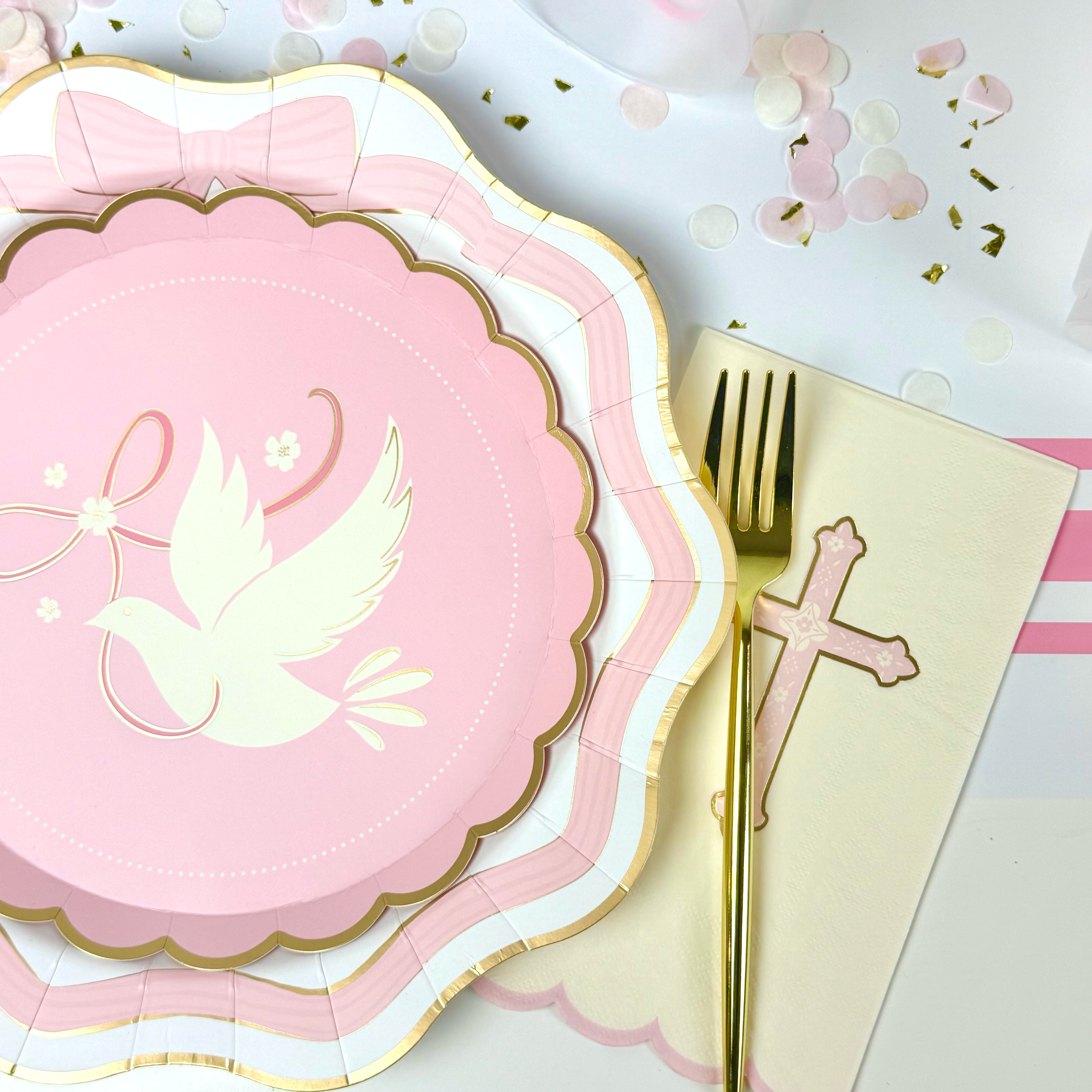 Pink scalloped paper plate with gold trim and a white dove design, styled with a gold fork, cross napkin, and pastel confetti.