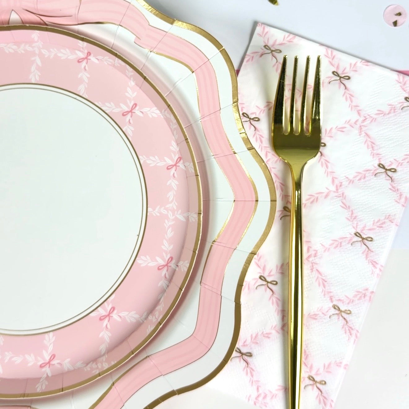 Pink trellis guest towel with small bow pattern styled beside pink scalloped plates and a gold fork.
