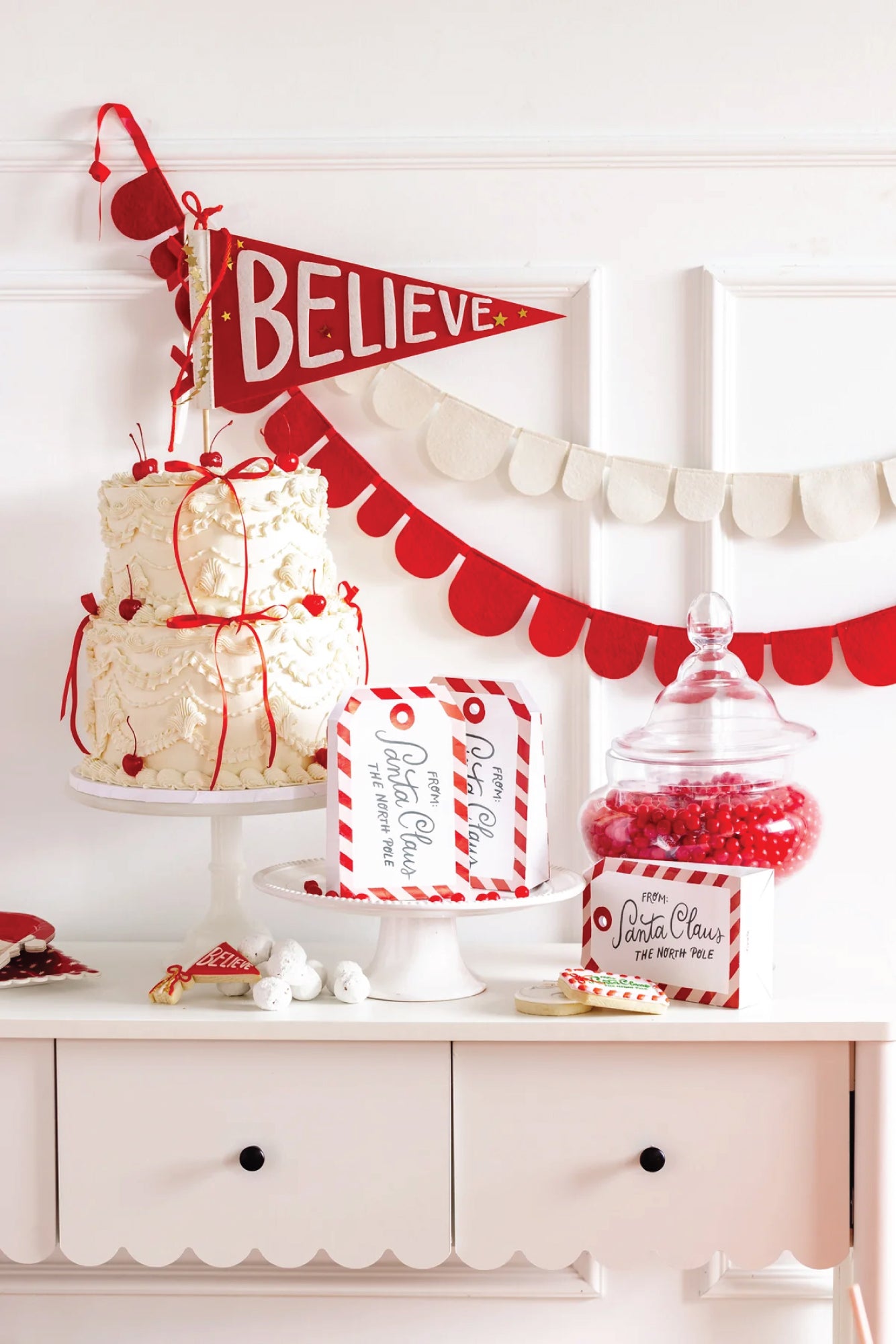 Decorative setup with a cake, candy, and 'Believe' pennant flag with Gift from Santa Claus Favor Bags