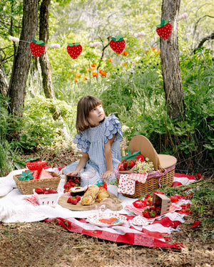 Child at a picnic in a forest with a basket of food and strawberry decorations.