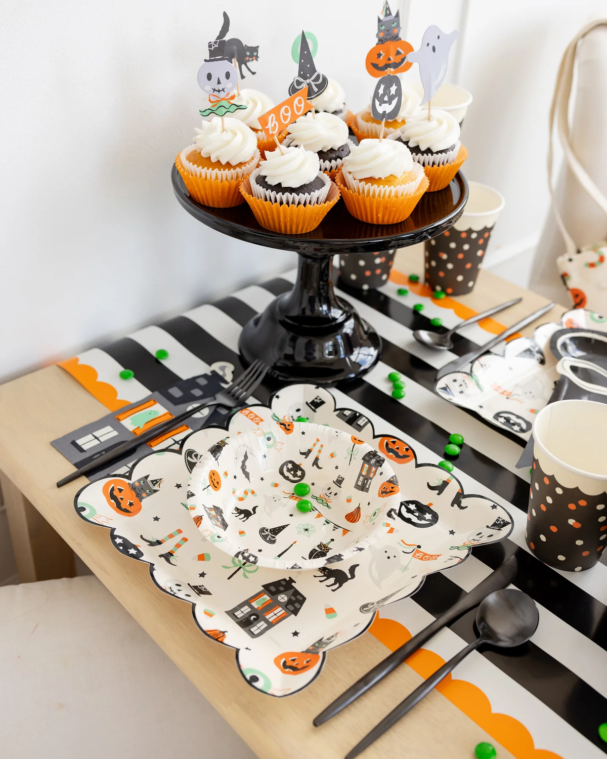 Halloween party table setting with Halloween cupcake toppers and decorative Halloween plates on a striped orange and black tablecloth.