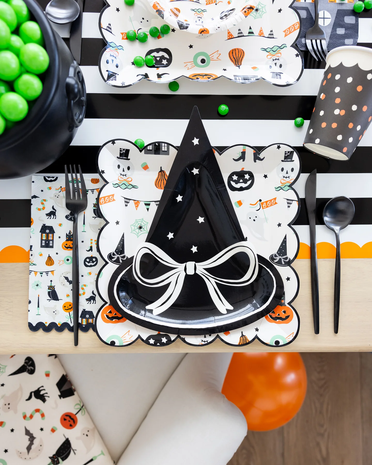 Halloween party table setting with a witch hat paper plate and black and white striped paper table cover