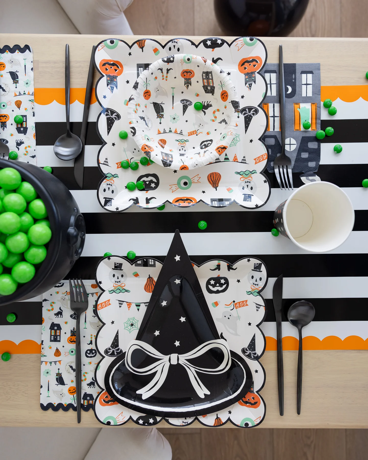 Halloween party table setting with decorative Halloween plates and utensils on a striped orange and black paper tablecloth.