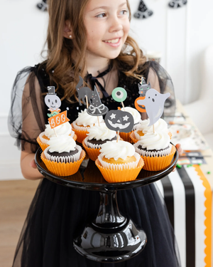 Girl holding a black cake stand with cupcakes topped with Halloween party picks