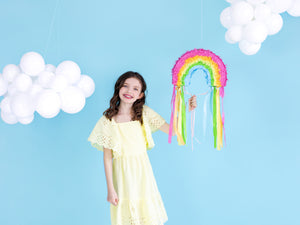 Girl with rainbow piñata and balloon clouds